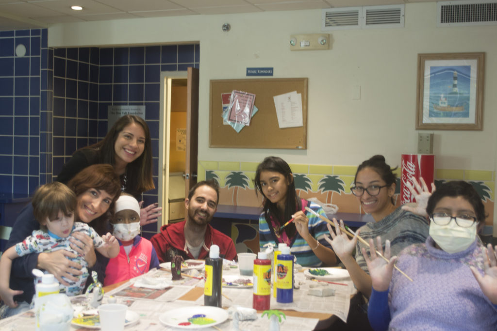 Group of volunteers and children sitting around a table with paints and paintbrushes during a painting activity at the Ronald McDonald Charity House in Miami