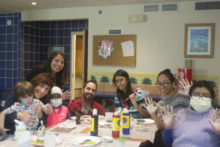 Group of volunteers and children sitting around a table with paints and paintbrushes during a painting activity at the Ronald McDonald Charity House in Miami