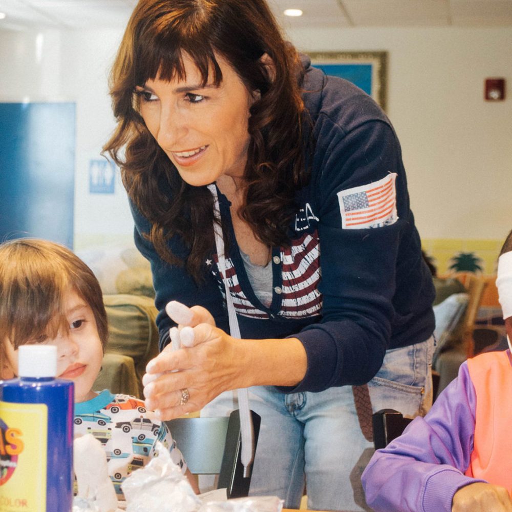 Photograph of founder Lia rolling clay with her hands while standing over a table with young children
