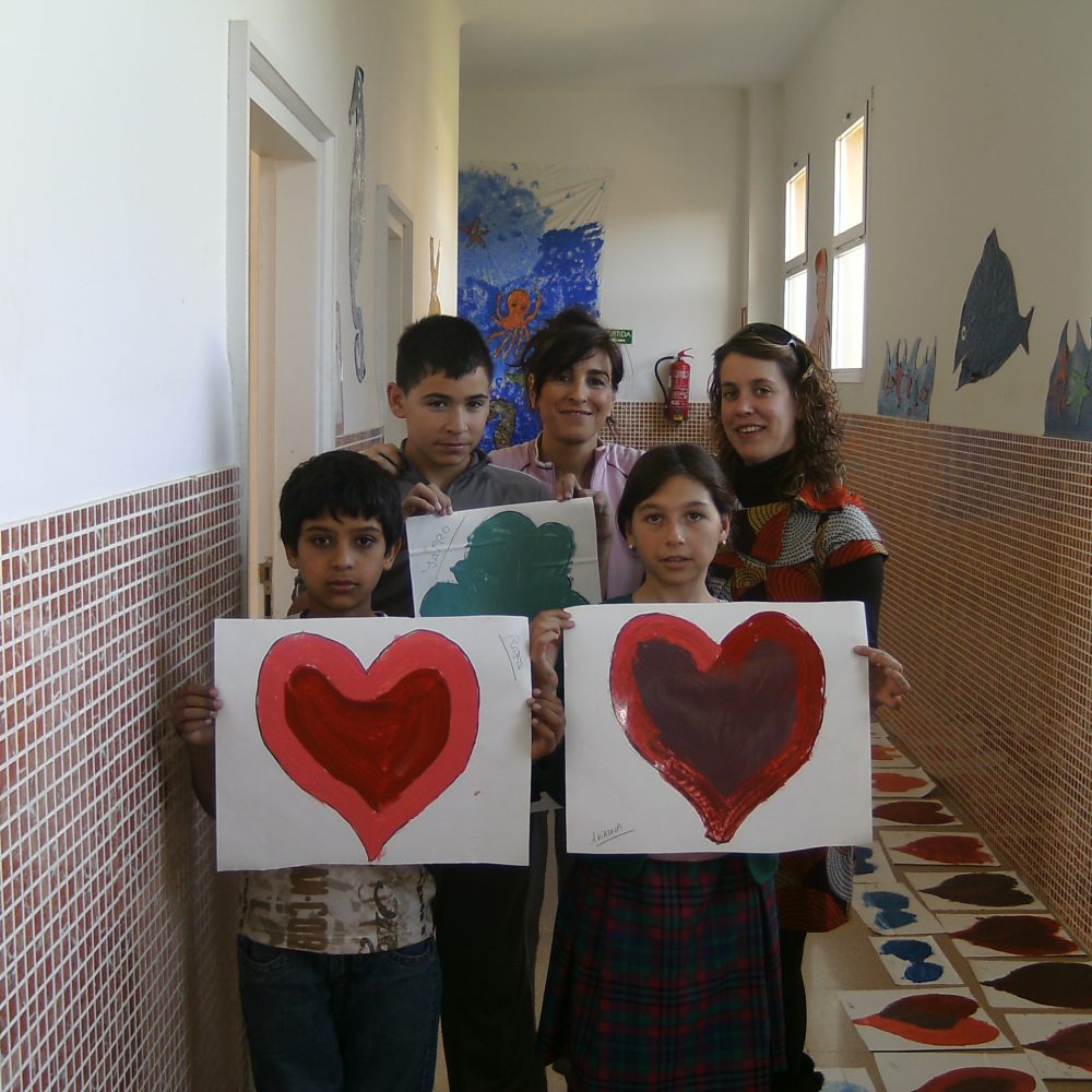Photograph of found Lia with a group of children standing in hallway of school holding up their paintings of hearts